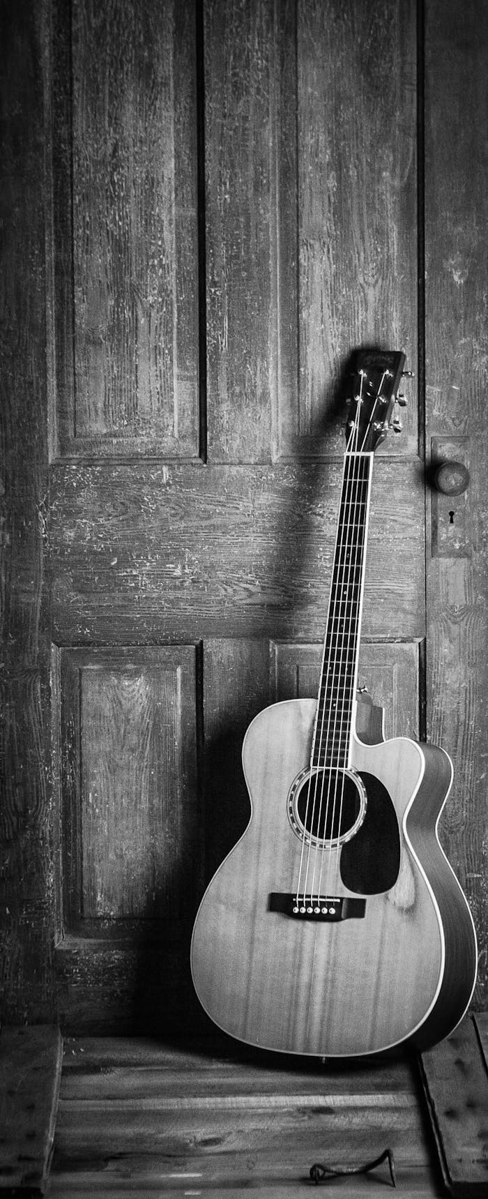 Home A classic acoustic guitar leaning against a rustic wooden door in a black and white vintage style.